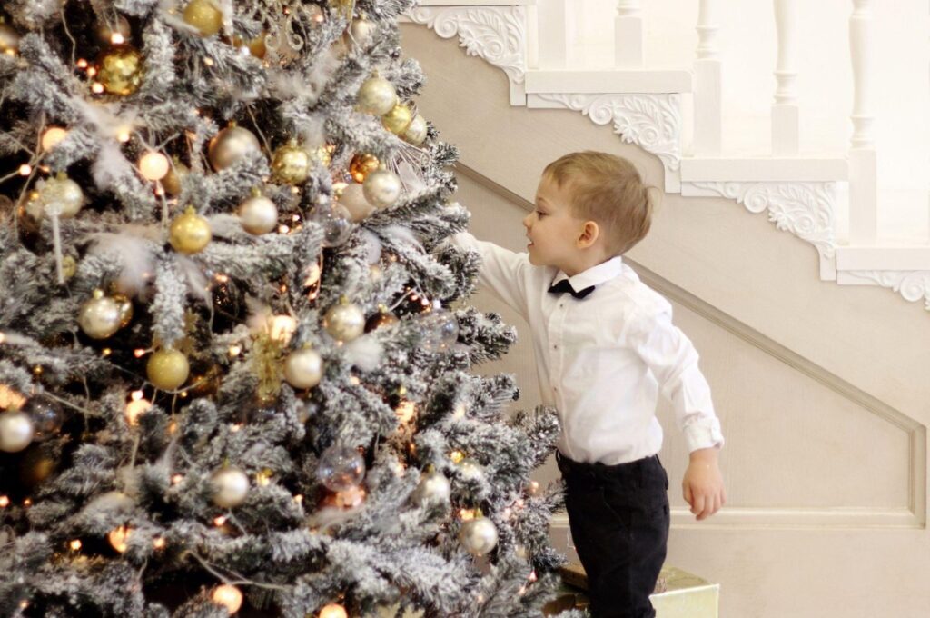 A kid in suit is decorating Christmas tree, beige tones